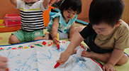 大きな紙にお絵描きをする子どもたち